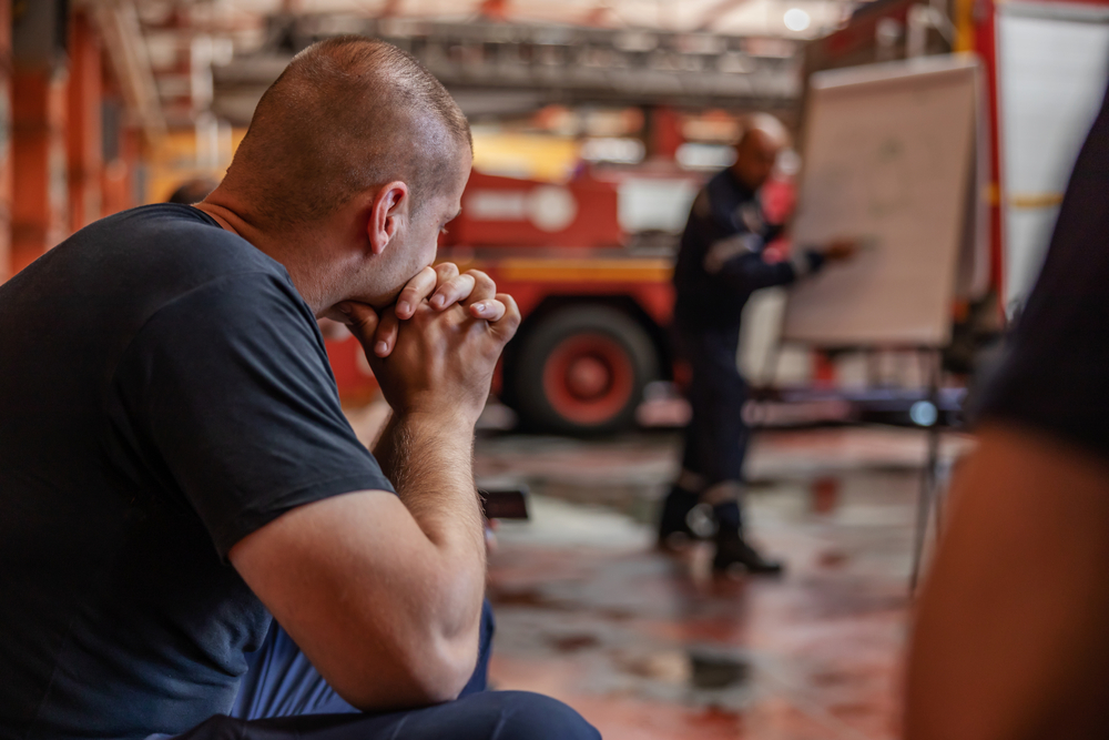 A first responder sits with hands clasped in thought during a station debrief.
